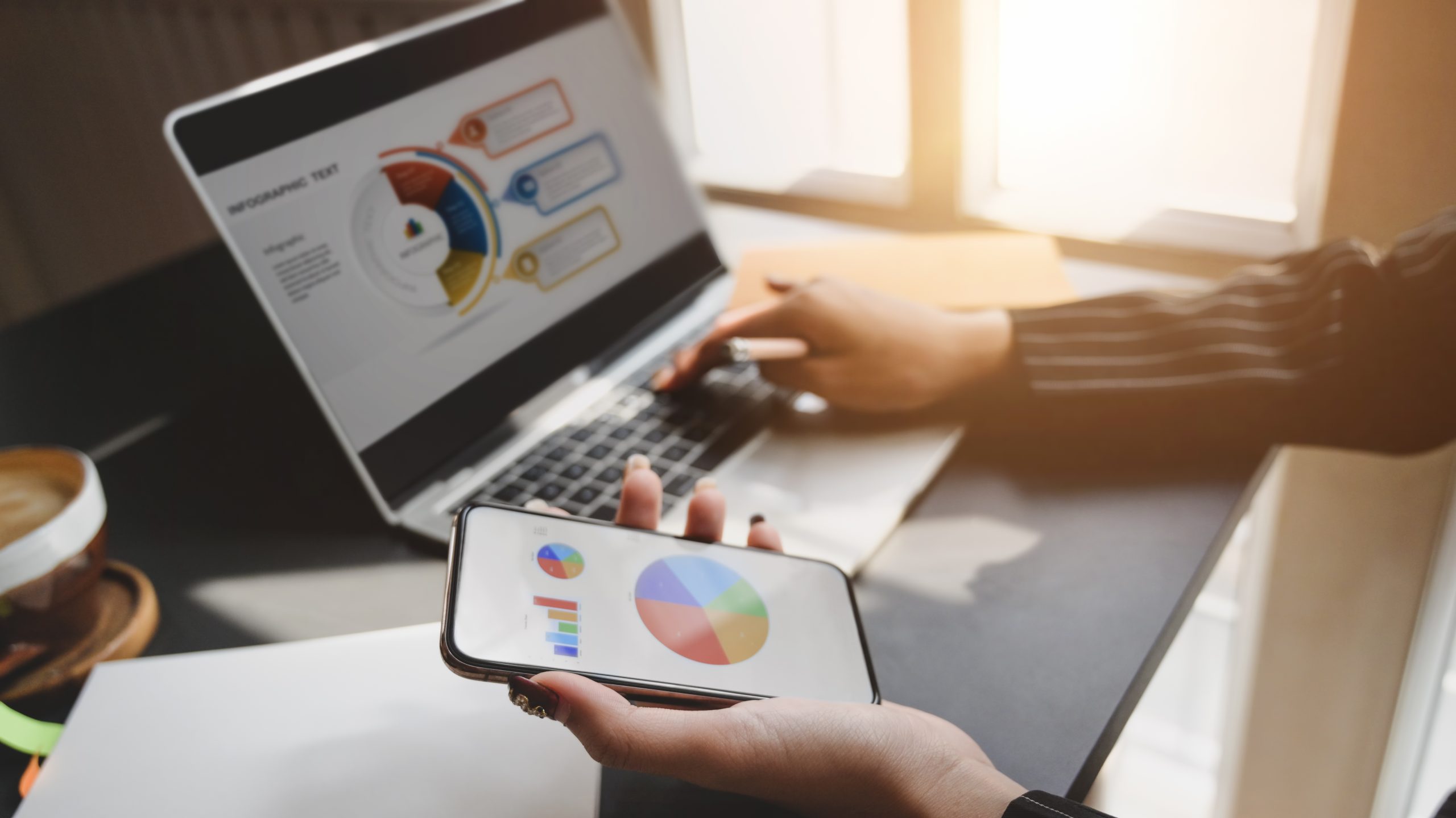 Cropped shot of businesswoman working on laptop while looking business chart on smartphone